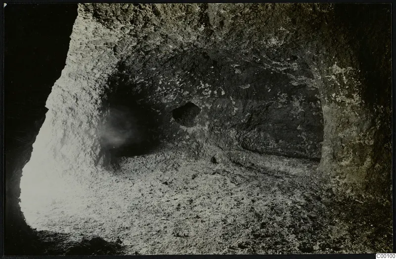 Interior of rock-cut Tomb 322 b at Lapithos, with a rough rock-cut chamber wall and a loose stony floor
