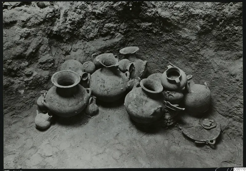Tomb chamber at Lapithos with a group of clay vessels set against the earth wall.