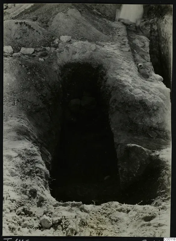 Tomb 416 at Lapithos Kastros during excavation, showing a rectangular opening in the ground with stones inside the dark chamber.