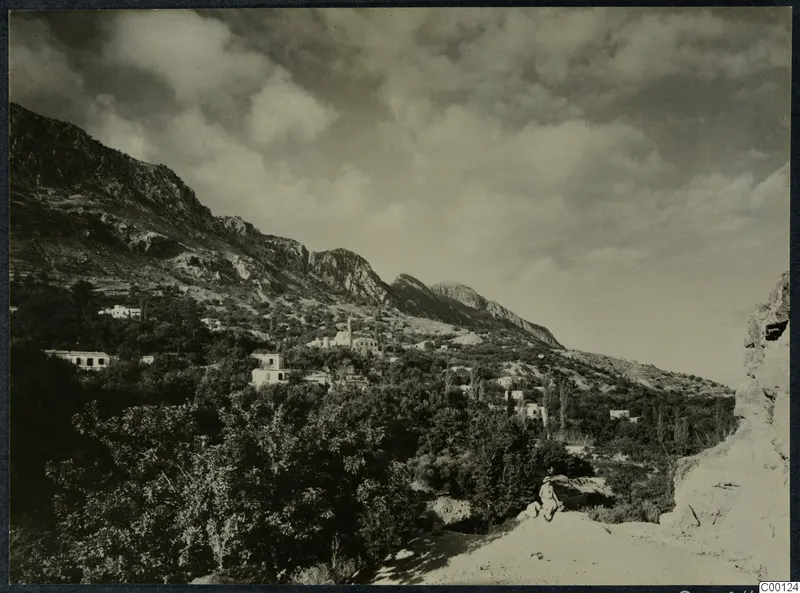Hillside village of white houses below a rocky mountain ridge, Lapithos, with a seated figure on a rock in the foreground