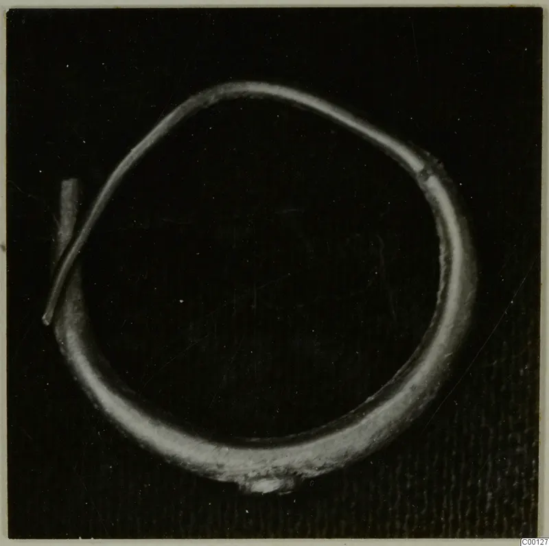 Gold earring: an open metal hoop with one tapering end, photographed on a dark background.