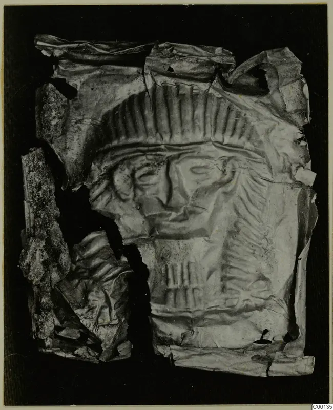 Torn, crumpled thin metal sheet with an embossed face and rows of ridges, Bronze Age gold and silver