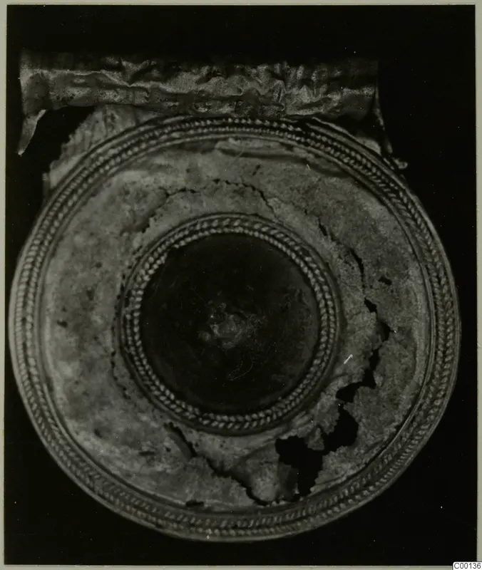 Gold round object from Lapithos Kastros tombs, seen from above, with a twisted-cord border and central boss.