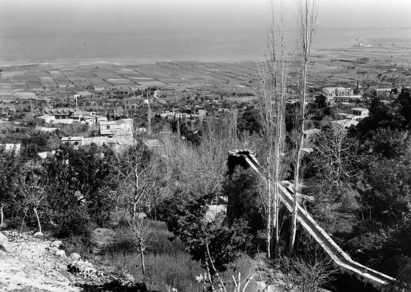 Landscape view from high ground over a village and rectangular fields, with the sea on the horizon beyond