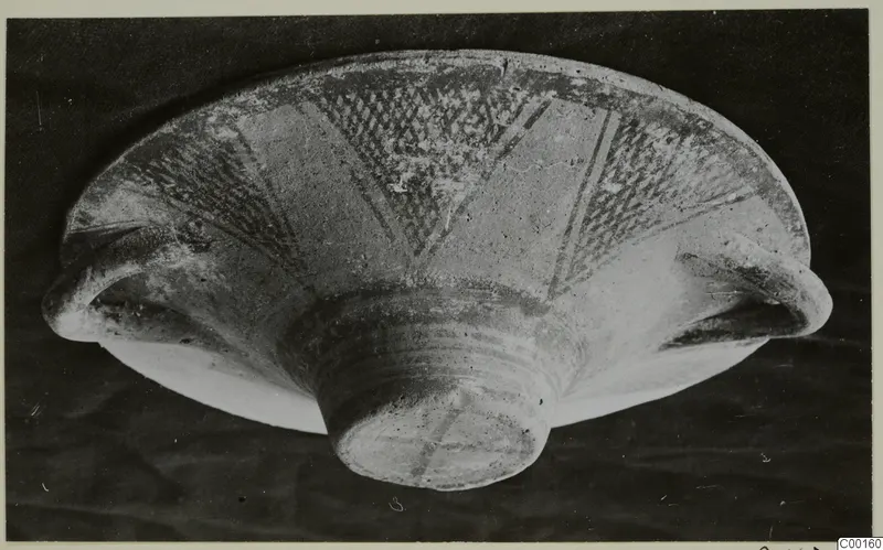 White Painted I bowl from Lapithos, photographed at an angle with dark painted hatched bands on its pale surface