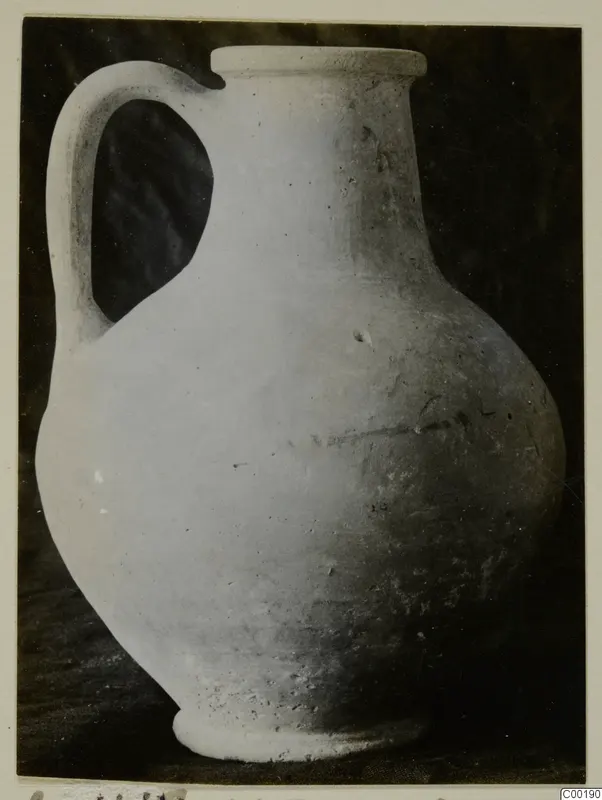 Plain white jug with a strap handle and a flat-topped rim, photographed against a dark background.