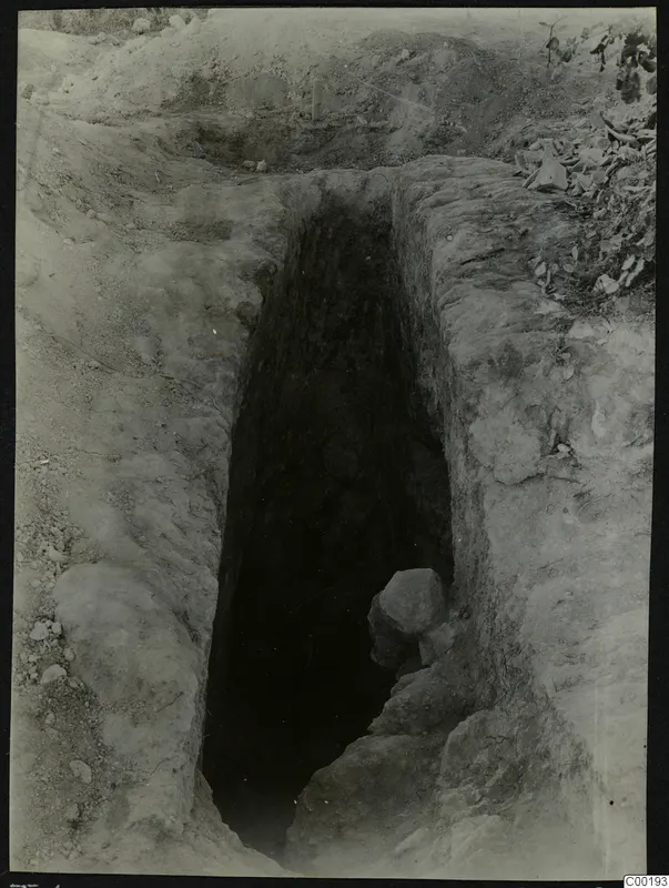 Tomb 408 at Lapithos Kastros during excavation, a deep narrow shaft cut into the earth with stones inside.