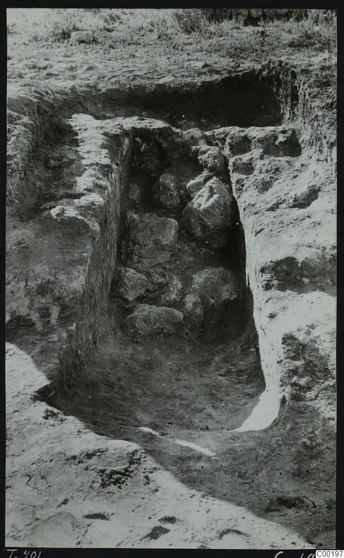 Tomb 401 at Lapithos Kastros during excavation, with large stones lying in the cut chamber among the soil.