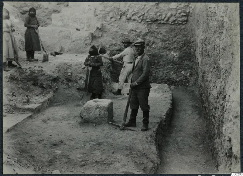 Workers with a pick and shovels in an excavation trench at Soli, with a large stone block and cut walls behind
