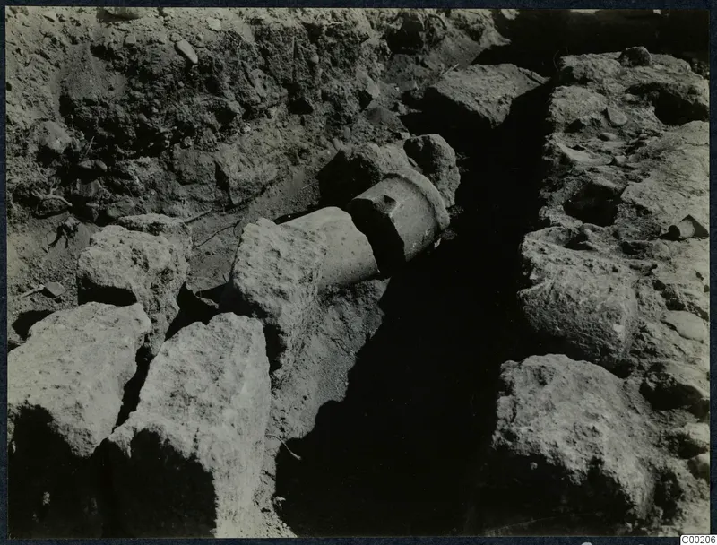 Excavation trench at Soli with large stone blocks on either side and a cylindrical stone piece lying across it
