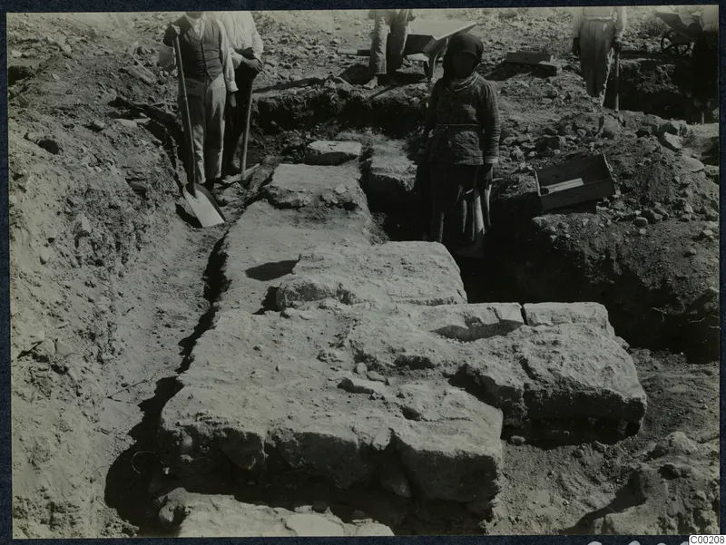 Excavation at Soli with workers, shovels and a wheelbarrow beside exposed large stone blocks in a trench