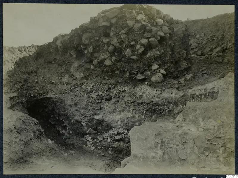 Excavation at the theatre at Soli, with a mound of stones above layers of soil and a pale cut rock face at right.