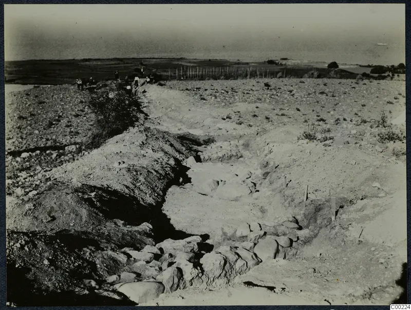 Excavation trench at Soli with stones along its floor and a group of people standing on the far rim