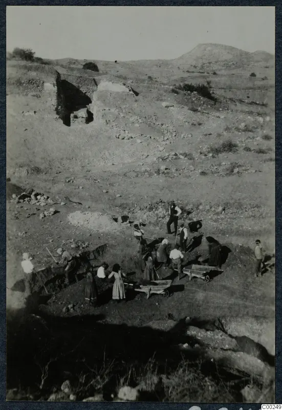 Excavation of the theatre at Soli, with workers digging and two wheelbarrows in use on a dry hillside
