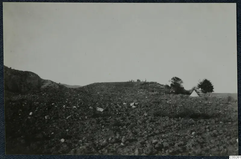 Stony hillside at Soli with a few small figures on the ridge top and a white tent beside a tree