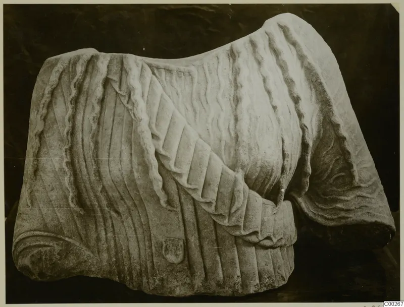 Marble sculpture fragment from Galini showing pleated drapery over the shoulder and wavy hair, seen from the front.