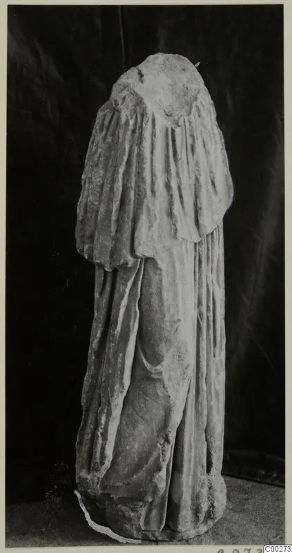 Draped marble sculpture of a standing figure, head missing, photographed against a dark backdrop