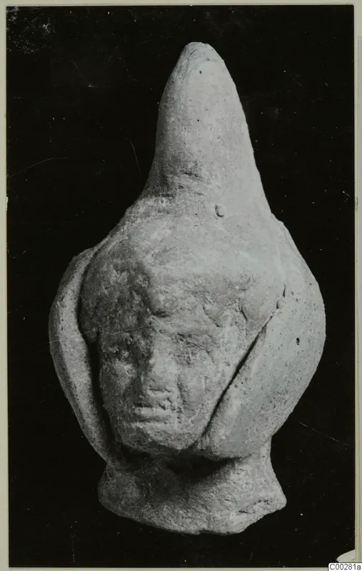 Small terracotta figurine with a tall pointed top and a worn human face, photographed against a dark background.