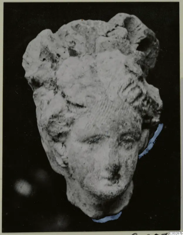 Terracotta head of a small figure with piled hair, photographed against a black background