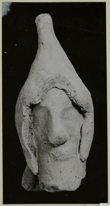 Terracotta Minor Plastic 3, a small terracotta figurine of a head with a tall tapering top, from Soli, against a black background.