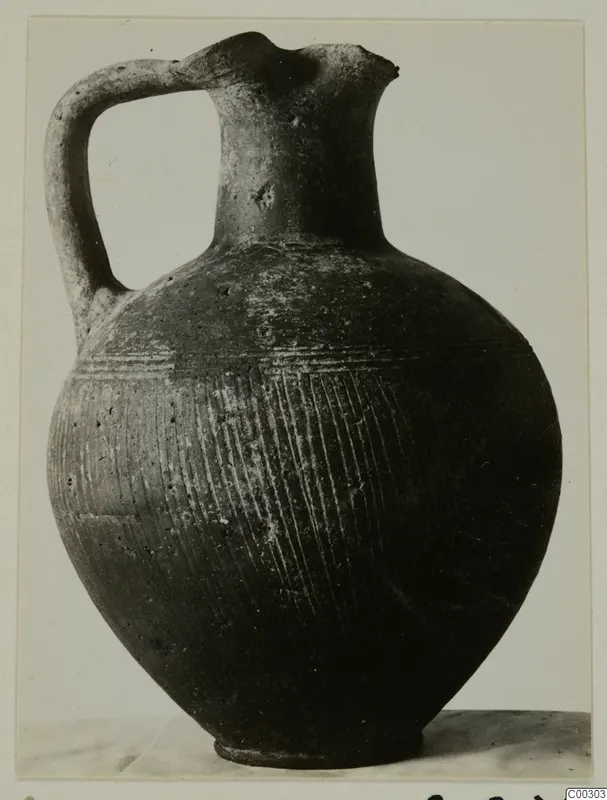 Pottery jug with a strap handle, a pinched mouth and closely spaced incised lines on its body