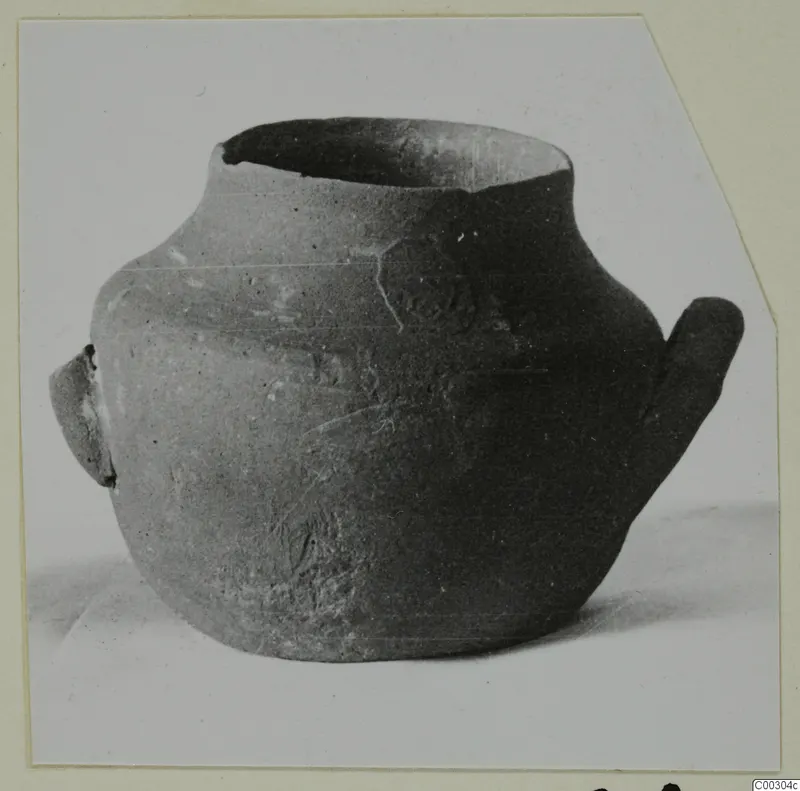 Black-slipped pottery jug with a wide mouth, a small lug handle on the left and a tall loop handle on the right.