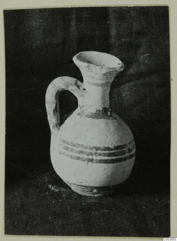 Small white-slipped jug with a loop handle and dark painted bands, photographed against a dark cloth.