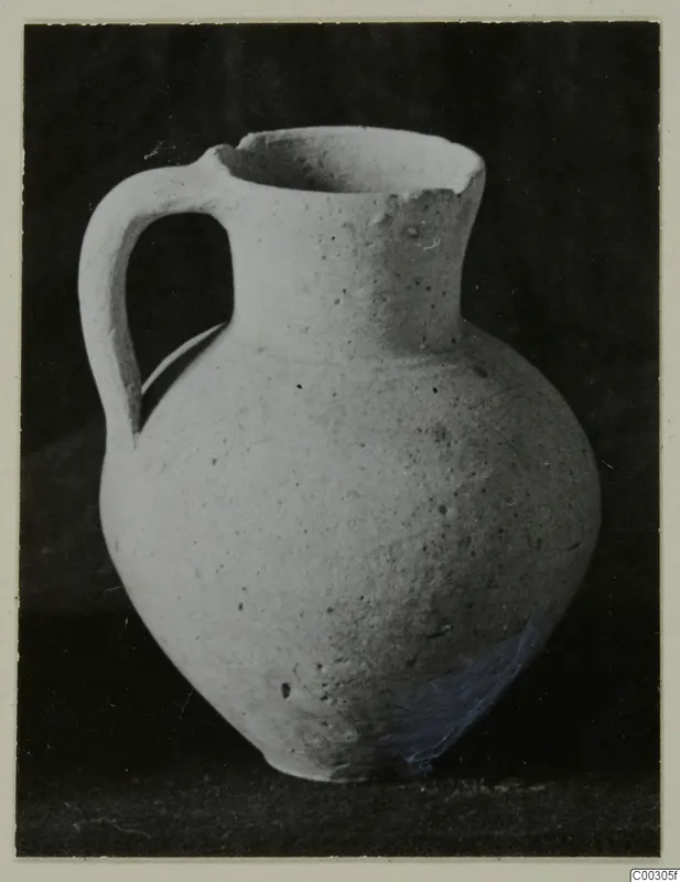 Pale pottery jug with a single loop handle, photographed against a dark background