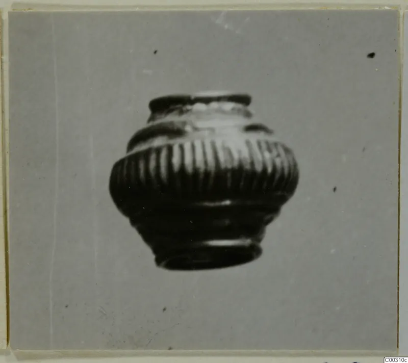 Small ribbed jar with a narrow mouth and moulded bands around the shoulder, photographed on a grey background