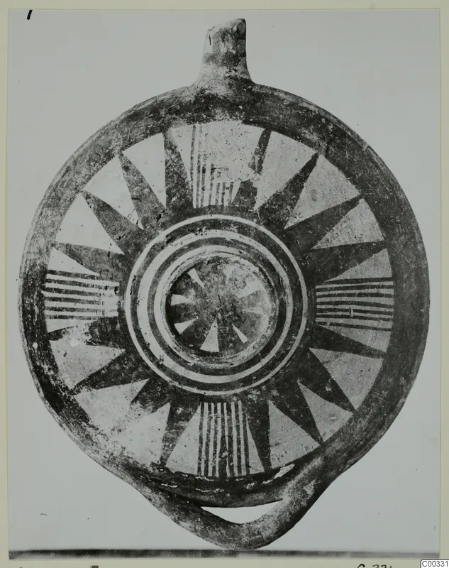 Round pottery vessel with a nozzle-like projection and loop handle, painted with dark radiating wedges and concentric rings