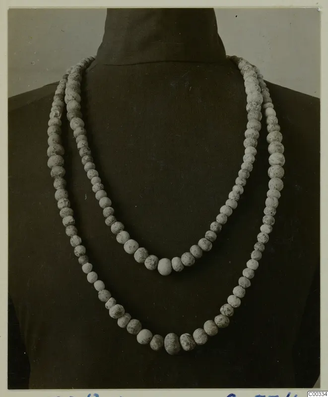 Two strands of pale, speckled beads draped over a dark stand, from the Lapithos Vrysi tou Barba tombs