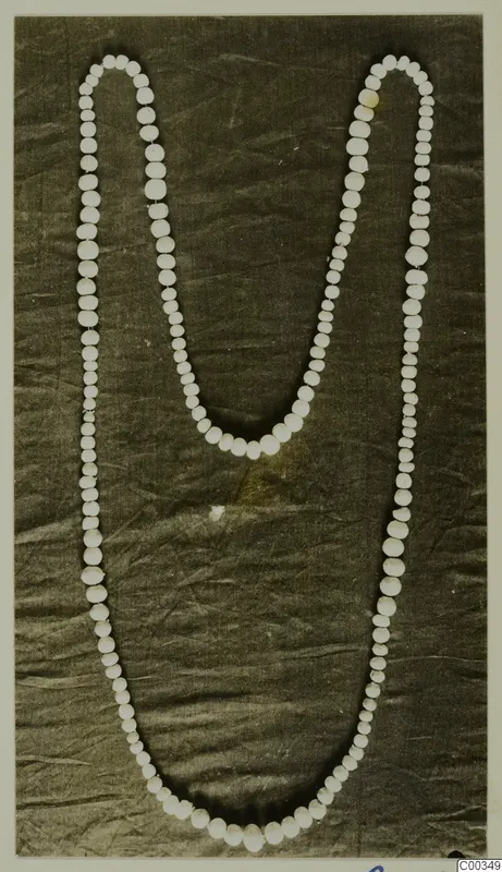 Necklace of pale round beads of varying sizes laid out on dark crumpled cloth