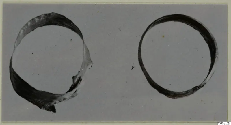 Two gold rings of band form, one broken, photographed on a grey background, from the Kastros tombs at Lapithos