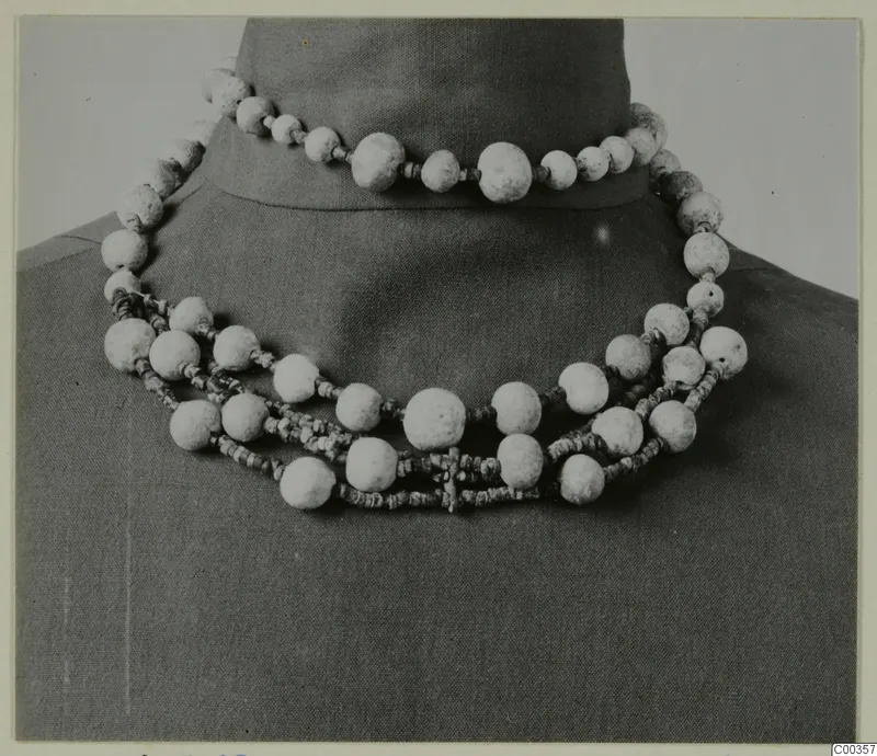 Necklace of large pale beads and small dark beads, draped over a dark bust, from the Lapithos Vrysi tou Barba tombs