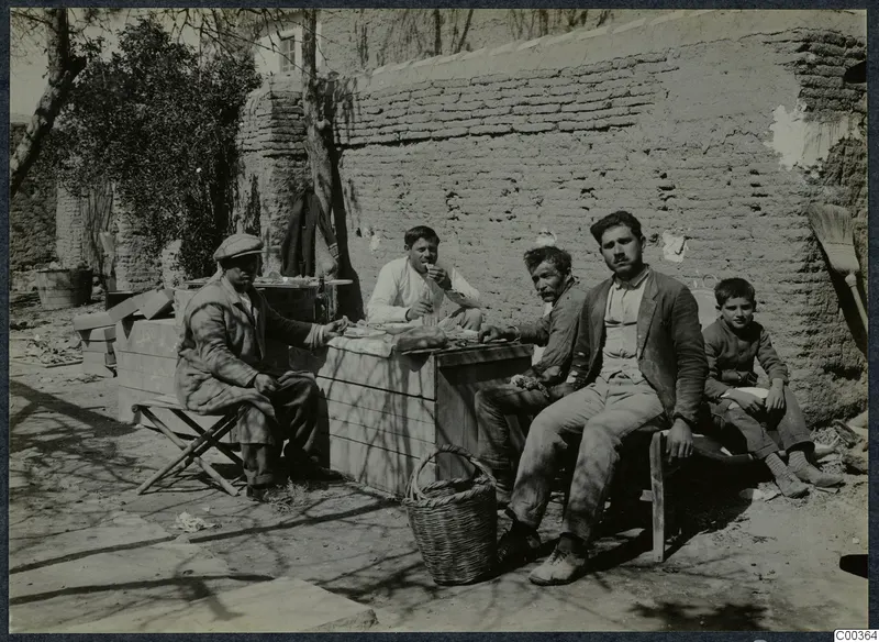Four men and a boy take a break at a wooden table outside a mud-brick wall.