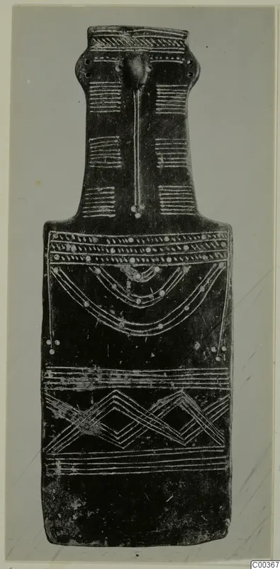Dark flat idol with a long neck and a raised ridge down the front, decorated with white incised bands, dots, arcs and zigzags