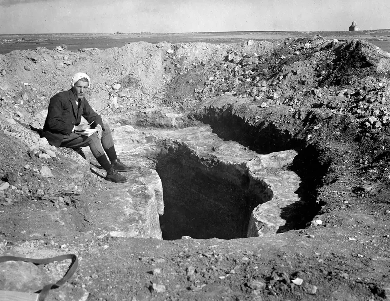 Alfred Westholm seated on the edge of a dromos excavation at Milia, holding a notebook