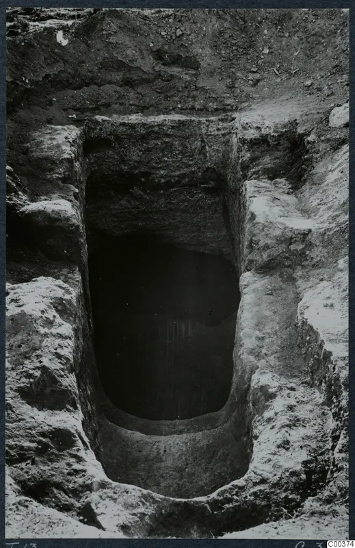 Tomb 13 at Milia during excavation, looking down into the dark opening of a rock-cut tomb chamber.