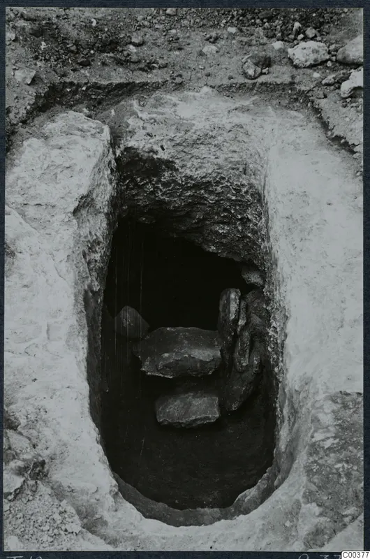 Rock-cut tomb 10 at Milia seen from above during excavation, with flat stone slabs inside the chamber opening