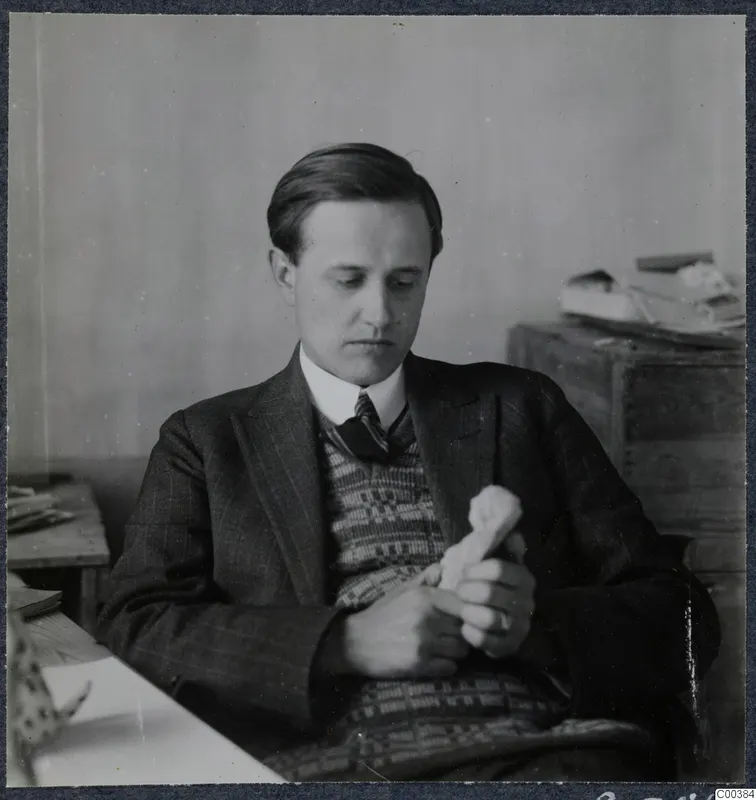 Einar Gjerstad seated at a desk, holding and looking down at a small pale object in his hands.