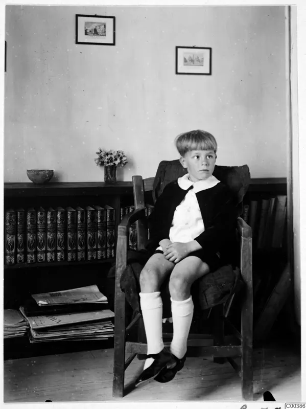 Martin Gjerstad seated in a wooden armchair beside a bookcase of leather-bound books, on Gladstone Rd