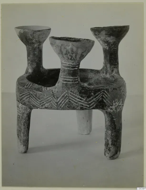 Red Polished pottery tripod vessel with three flaring bowl-shaped mouths on tall necks, set on three short legs.