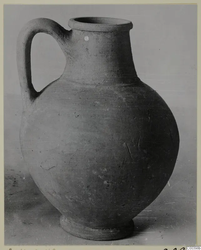 Plain pottery jug with a single loop handle and wide mouth, photographed against a plain grey backdrop