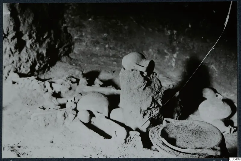 Tomb 11 at Milia: tomb chamber during excavation, with pottery vessels and bones lying on the floor.