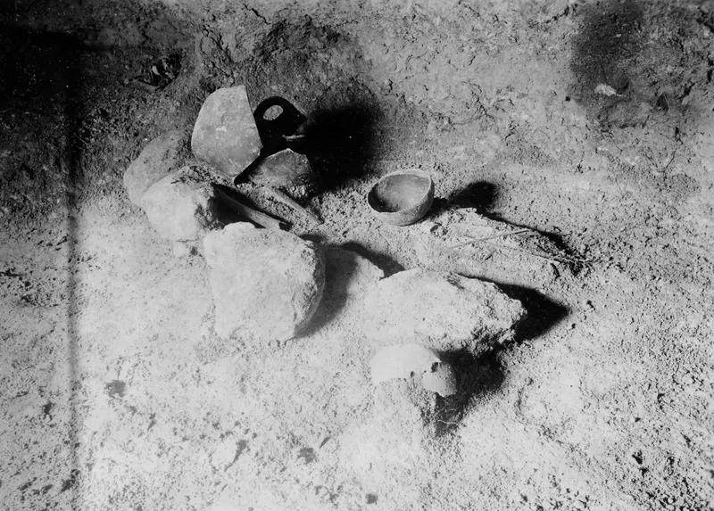 Tomb 317 interior at Lapithos, with broken pottery, a small bowl and large stones on the earthen floor
