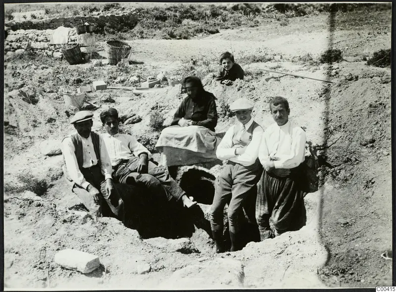 Excavation at Lapithos with baskets and a group of adults and a child posed in and around a pit