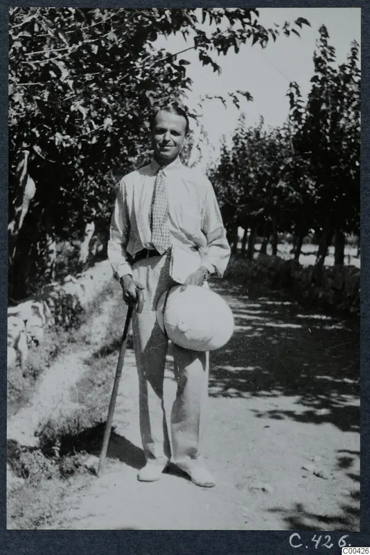 Erik Sjöqvist standing on a shady track at Lapithos, holding a walking stick and a pale hat.