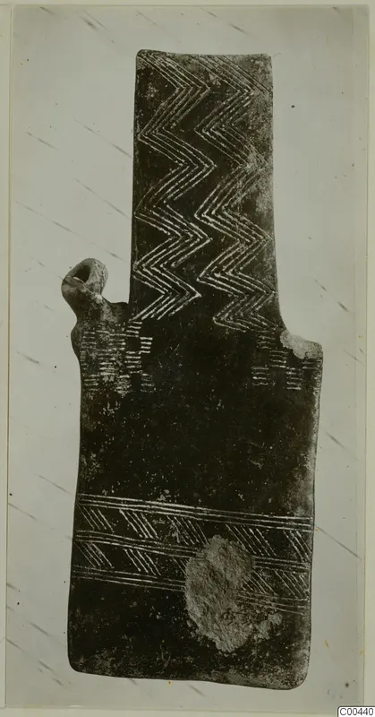Plank-shaped figurine, back view, with incised zigzag and chevron patterns on a dark surface.