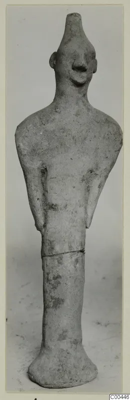 Standing terracotta figurine with a tall cylindrical head, pinched nose and arms held close to the body, seen from the front.