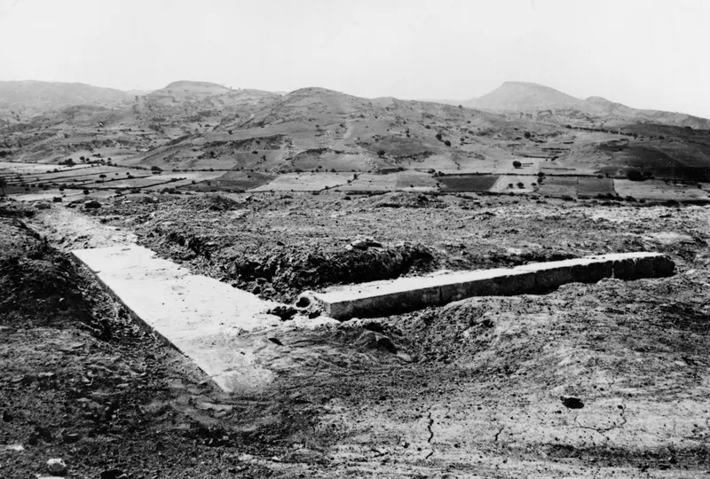 Excavated terrace at Soli with long stone foundation walls, hills and cultivated fields beyond.